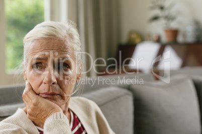 Active senior woman with hand on face sitting on sofa in a comfortable home