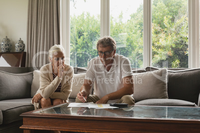 Active senior couple calculating domestic bills on sofa in living room