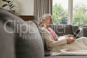 Active senior woman relaxing on sofa and using laptop in living room at comfortable home