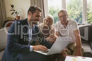 Active senior couple discussing with real estate agent over laptop in living room