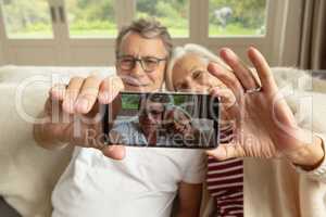 Active senior couple sitting on sofa and taking selfie in a comfortable home