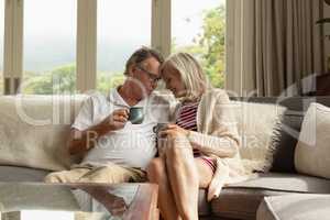 Romantic active senior couple having coffee on sofa in a comfortable home