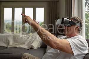 Active senior man using virtual reality headset on sofa in a comfortable home