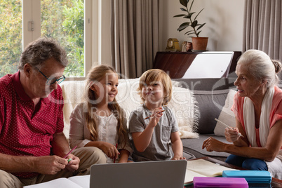 Grandparents helping grandchildren with homework in living room at comfortable home