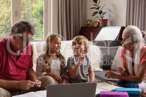 Grandparents helping grandchildren with homework in living room at comfortable home