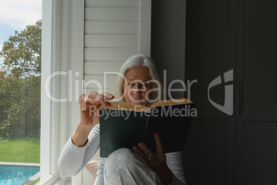 Active senior woman reading a book on window seat