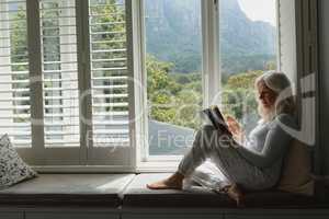 Active senior woman reading a book on window seat