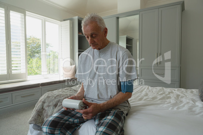 Active senior man measuring blood pressure with sphygmomanometer in bedroom