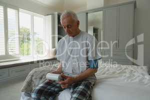 Active senior man measuring blood pressure with sphygmomanometer in bedroom