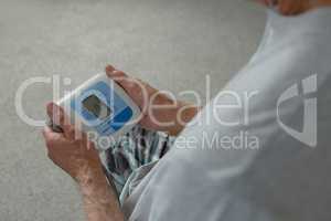 Active senior man measuring blood pressure with sphygmomanometer in bedroom at home