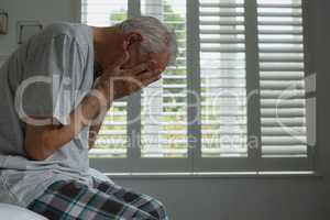 Active senior man covering face with hands in bedroom