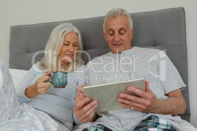 Active senior couple using digital tablet in bedroom