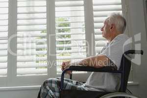 Active senior man in wheelchair looking through window at home