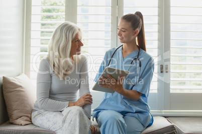 Active senior woman and female doctor using digital tablet on window seat