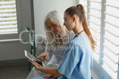 Active senior woman and female doctor using digital tablet on window seat