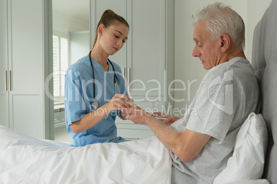 Female doctor giving medicine to active senior patient in bedroom