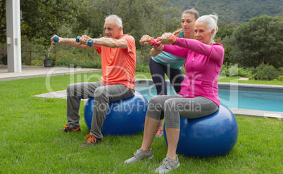 Female trainer assisting active senior couple to exercise with dumbbells