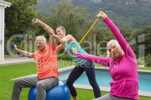 Female trainer assisting active senior couple to exercise with resistance band