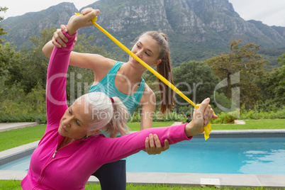 Female trainer assisting active senior woman to exercise with resistance band