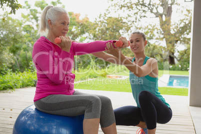 Female trainer assisting active senior woman to exercise with dumbbells in the porch