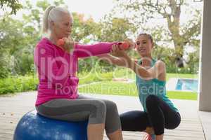 Female trainer assisting active senior woman to exercise with dumbbells in the porch