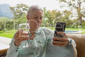 Active senior woman using mobile phone having champagne in the porch