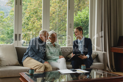 Active senior couple discussing with real estate agent over documents in living room