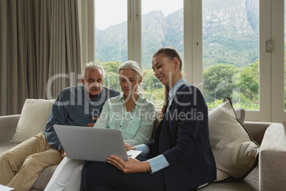 Active senior couple discussing with real estate agent over laptop in living room