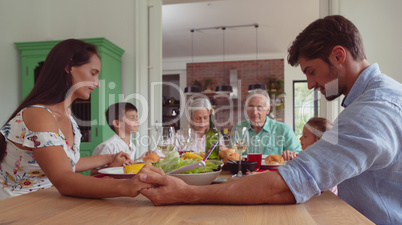 Multi-generation family praying before having food on dining table