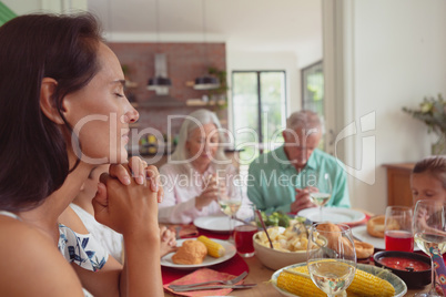 Multi-generation family praying before having food on dining table