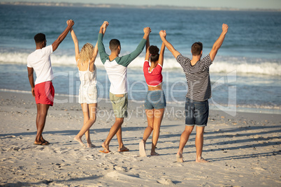 Group of friends standing with raised hands on the beach