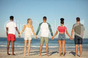 Group of friends standing together hand in hand on the beach