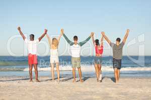 Group of friends standing together with hands raised on the beach