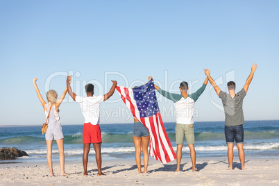Group of friends standing together with American flag and raising hands on the beach