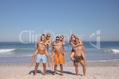 Male friends giving piggyback ride to female friends on the beach