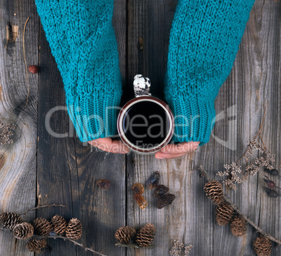 female hands in a green knitted sweater holding a ceramic mug wi