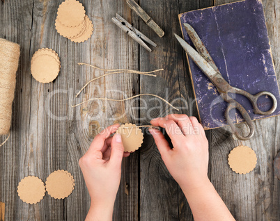 two female hands and paper tags with a brown rope on a gray wood