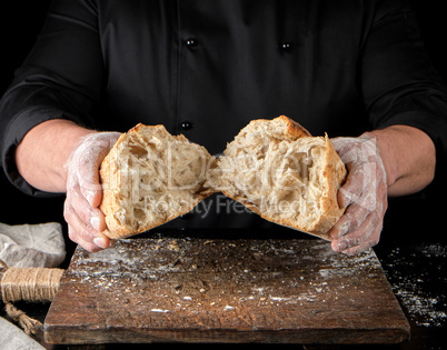 baker in black uniform broke in half a whole baked loaf of white