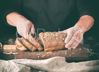 baker cuts a knife into slices of rye bread with pumpkin seeds