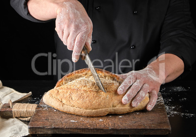 chef in black uniform cuts baked white wheat flour oval bread