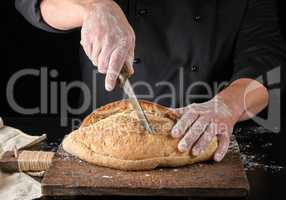 chef in black uniform cuts baked white wheat flour oval bread