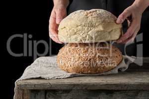 female hands holding round baked wheat flour bread over wooden t