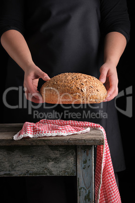 woman in a black apron holds in her hands baked round rye bread