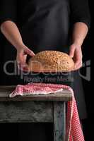 woman in a black apron holds in her hands baked round rye bread