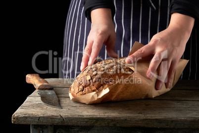 girl in black clothes wraps a whole baked loaf of bread in brown