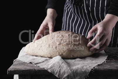 female hands holding oval baked wheat flour bread over wooden ta