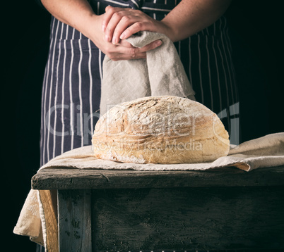 woman in an apron holds a gray linen napkin and round bread