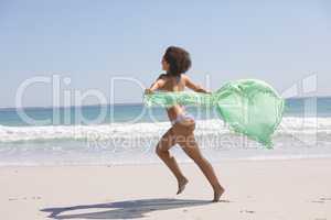 Woman in bikini with scarf running on the beach