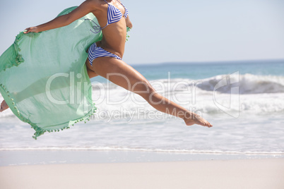 Woman in bikini with scarf jumping on the beach