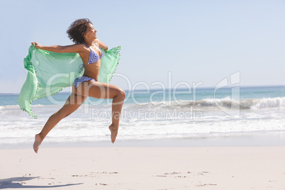 Woman in bikini with scarf jumping on the beach